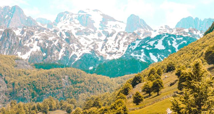 Los verdes valles de primavera contrastan con las cimas nevadas de los Alpes albaneses bajo un cielo brumoso.