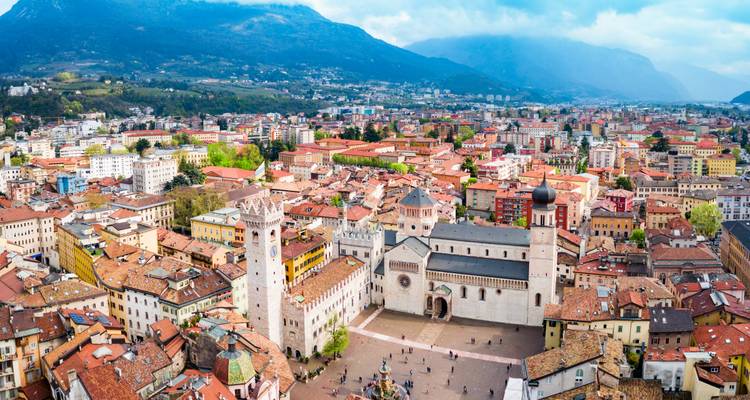 Panoramic aerial of Trento’s historic center with cathedral, square and surrounding mountains.