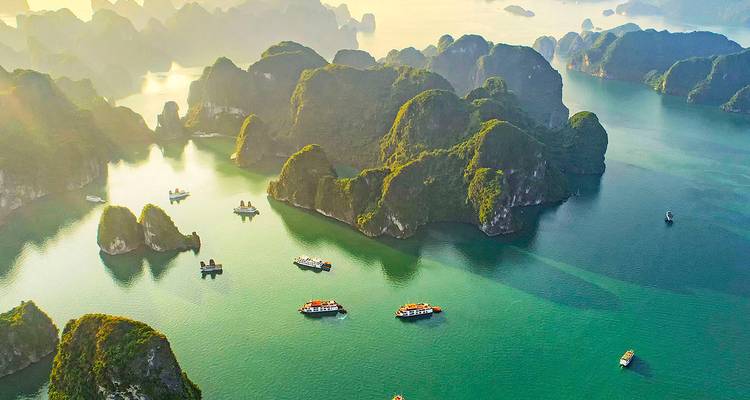 Aerial sunrise view of emerald waters and limestone islands of Halong Bay with cruise boats.