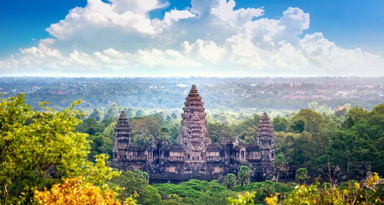 Angkor Wat’s iconic towers rise above jungle foliage on the horizon under a dramatic sky.