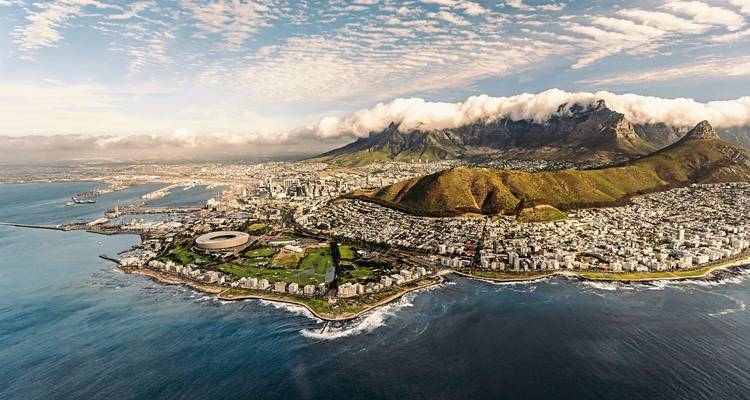 Sweeping helicopter view of Cape Town’s city bowl, stadium and dramatic mountains hugging the Atlantic shore.
