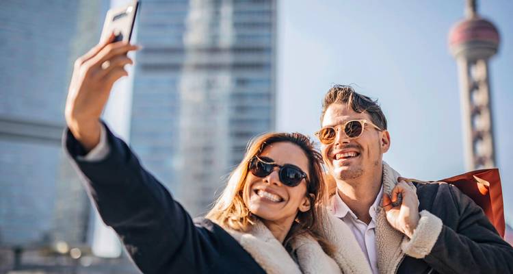 Lachendes Paar, das ein Selfie mit unscharfen modernen Wolkenkratzern und dem Oriental Pearl Tower im Hintergrund macht.