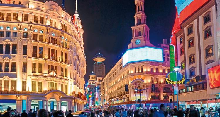 Lebendige Nachtszene der Nanjing Road in Shanghai mit historisch beleuchteten Gebäuden, Leuchtreklamen und belebten Menschenmengen.