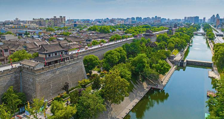 Luftaufnahme der antiken Stadtmauer von Xi'an neben einem grünen Wassergraben und der modernen Skyline in der Ferne.