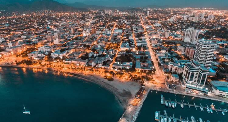 Aerial twilight view of Santa Marta city lights stretching from the waterfront toward distant mountains.