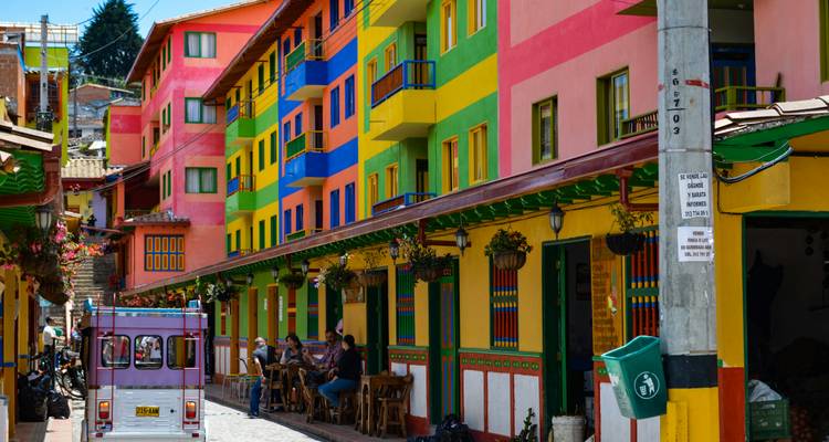A vivid street in Colombia with multicolored buildings, hanging baskets, and small cafés along the sidewalk.