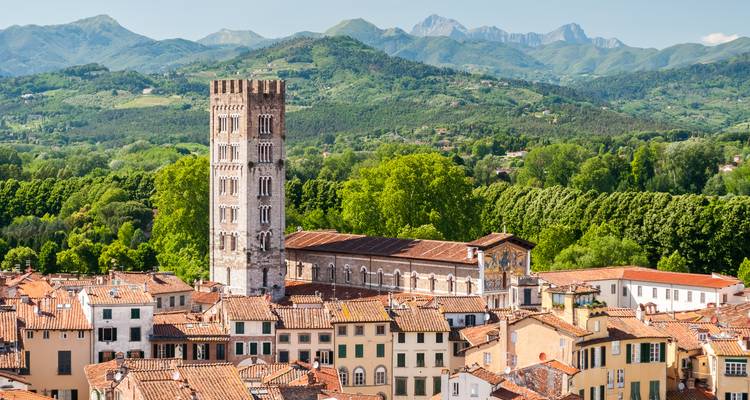 La tour médiévale de San Frediano s'élève au-dessus des toits en terre cuite de Lucques avec des montagnes boisées au-delà.