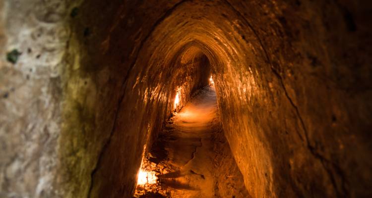 A dimly lit narrow tunnel carved through earth, part of the historic Cu Chi tunnel network.