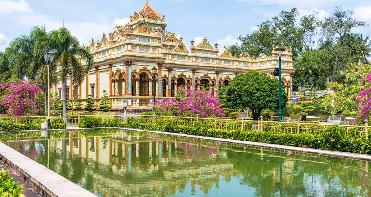 An ornate Buddhist temple with pink bougainvillea reflected in a rectangular pond in the Mekong Delta.