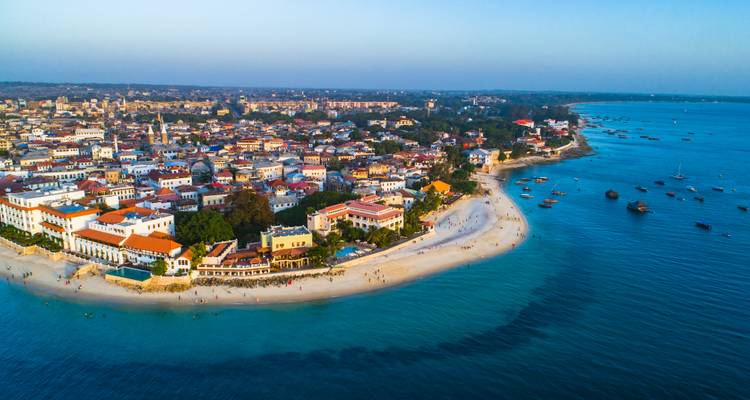 Drone view of Stone Town peninsula with sandy beaches, historic buildings and turquoise sea stretching along the coast.