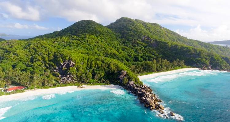 Aerial view of a lush green island with twin beaches and turquoise surf on either side.