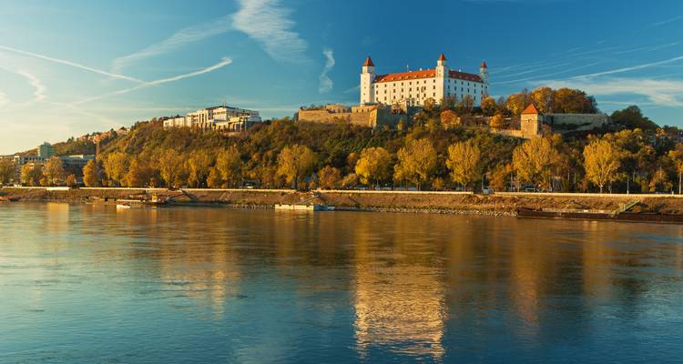 Le château de Bratislava se dresse au sommet d'une colline boisée dominant le Danube sous un ciel chaud en fin d'après-midi.