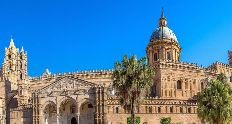 Facade and dome of Palermo Cathedral framed by palm trees against clear blue sky