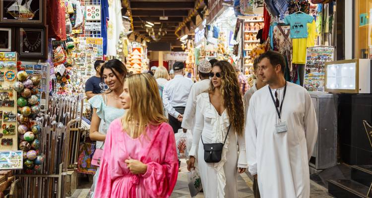 Winkelende bezoekers bladeren door kleurrijke kraampjes vol souvenirs in de drukke Muttrah Souq van Muscat.