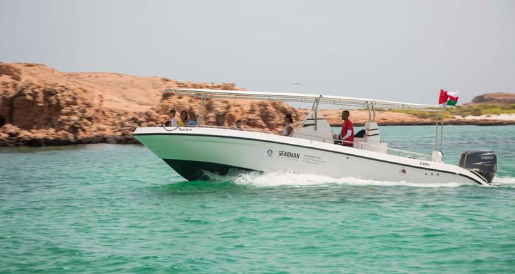 Een speedboat met toeristen scheert over turkooizen water langs een rotsachtige kust onder een heldere hemel.
