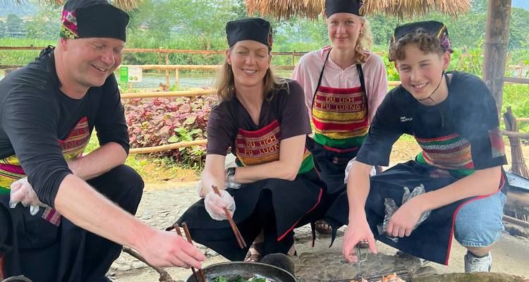 Family in traditional aprons cooks together over an outdoor wood fire in rural Vietnam.