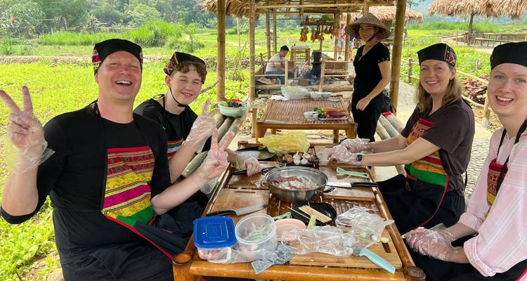 Group gathered around a rustic table preparing ingredients for a Vietnamese meal in an open hut.