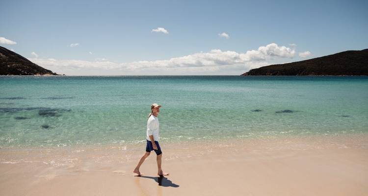 Man walking along a pristine white-sand beach beside turquoise Tasman Sea