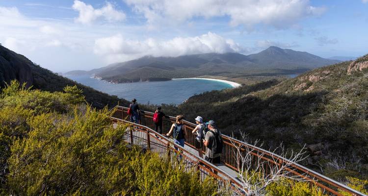 Hikers on a viewing platform overlooking the curved bay and mountains of Freycinet