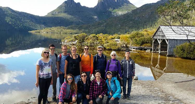 Tour group posing by a reflective alpine lake with Cradle Mountain backdrop