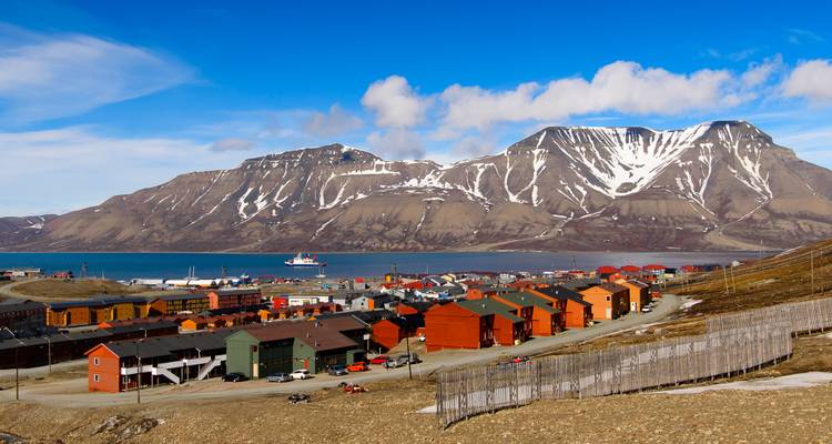 Panoramic view of Longyearbyen settlement hugged by rugged snow-striped mountains with a cruise ship in the bay.