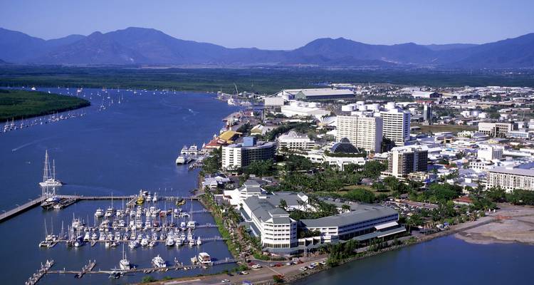 Vue aérienne de la marina de Cairns et de la ville dominée par des montagnes couvertes de forêt tropicale et un estuaire fluvial sinueux.