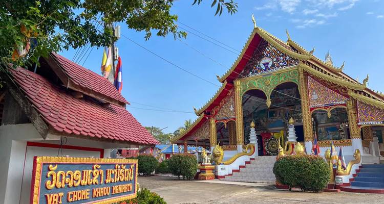 Kleurrijke tempel met rode dakpannen en sierlijk gouden details staat onder een helderblauwe hemel.