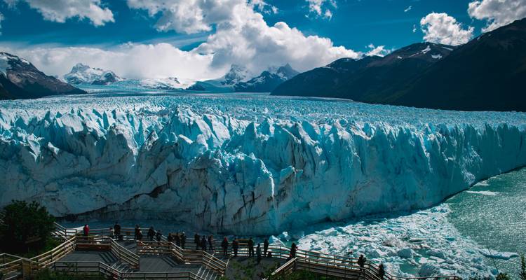 Weite Kante des Perito-Moreno-Gletschers, fotografiert von mehrstöckigen Holzplattformen, die mit Besuchern gefüllt sind.