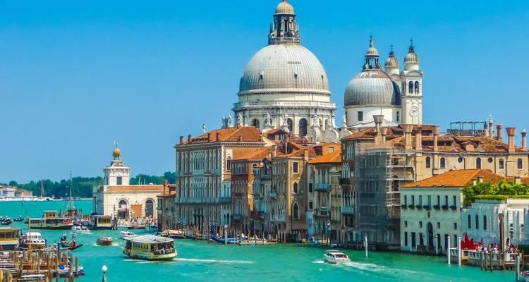 Tagesansicht entlang des Großkanals von Venedig mit der Basilika Santa Maria della Salute und verkehrsreichen Vaporettos, die türkisfarbene Gewässer befahren.