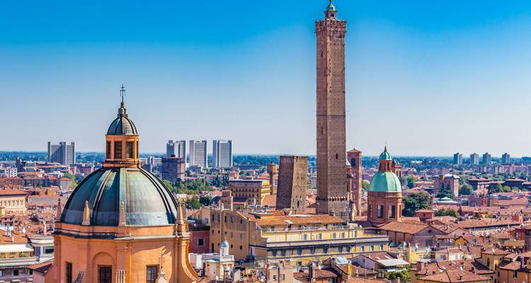 Panoramisch stadsaanzicht van Bologna met een koepelingskerk, de hoge Asinelli-toren en terracotta daken onder een heldere blauwe lucht.
