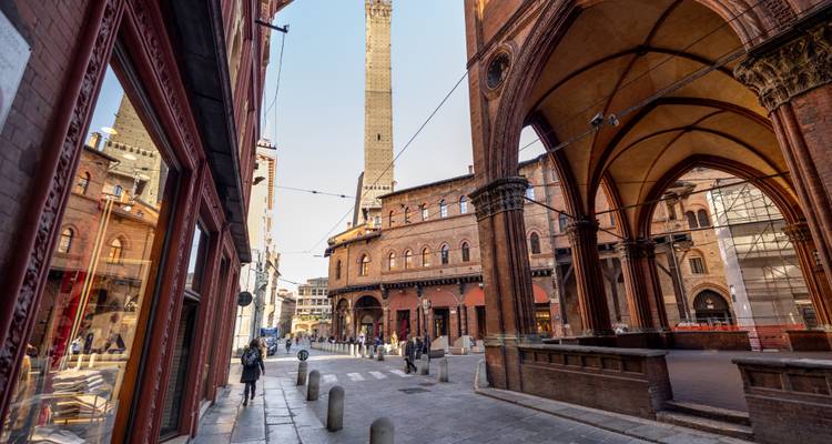 Straatscène onder Bologna's middeleeuwse galerijen met uitzicht op de Twee Torens; een paar voetgangers wandelen langs.