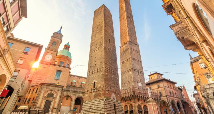 Warm zonsondergang licht dat Bologna's Twee Torens en omringende smalle straatjes met kerkkoepel op de achtergrond verlicht.