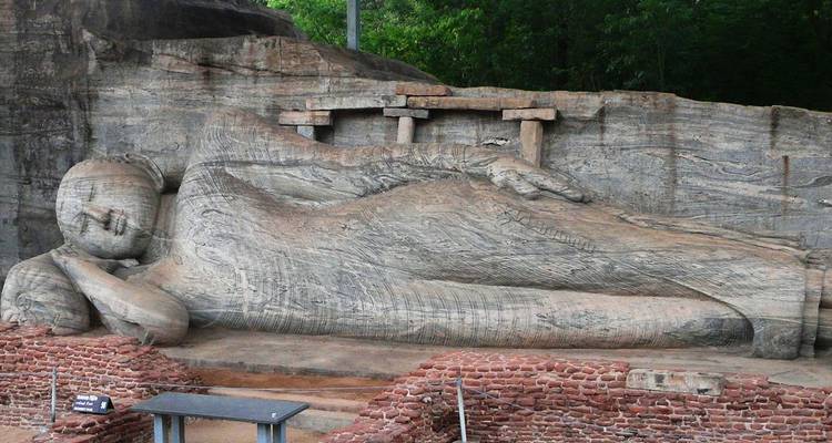 Massive antike liegende Buddha-Statue aus Granitstein in Gal Vihara, umgeben von Ruinen und Grünflächen.