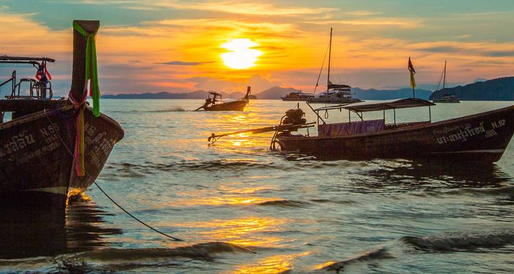 Des bateaux à queue longue se détachant en silhouette contre un coucher de soleil d'un orange vibrant sur les eaux calmes de la mer d'Andaman.