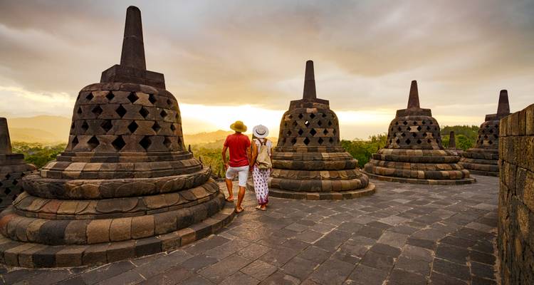 Couple walking among Borobudur’s bell-shaped stupas at sunrise with warm golden light