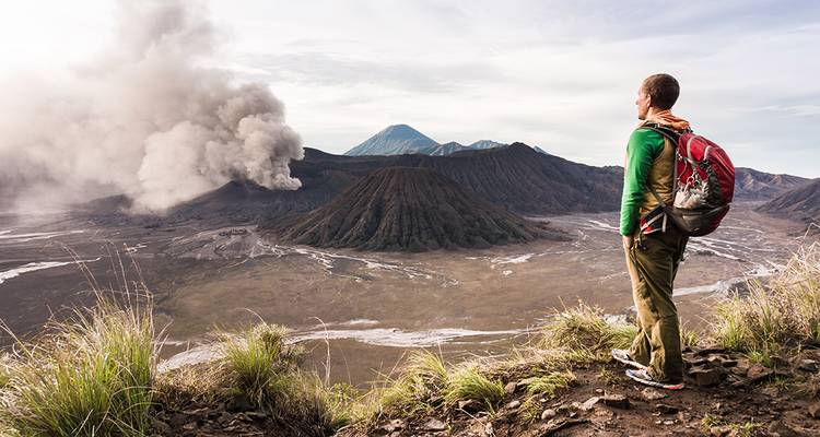 A backpacker watches volcanic ash rise from Mount Bromo on an adventurous rim hike.