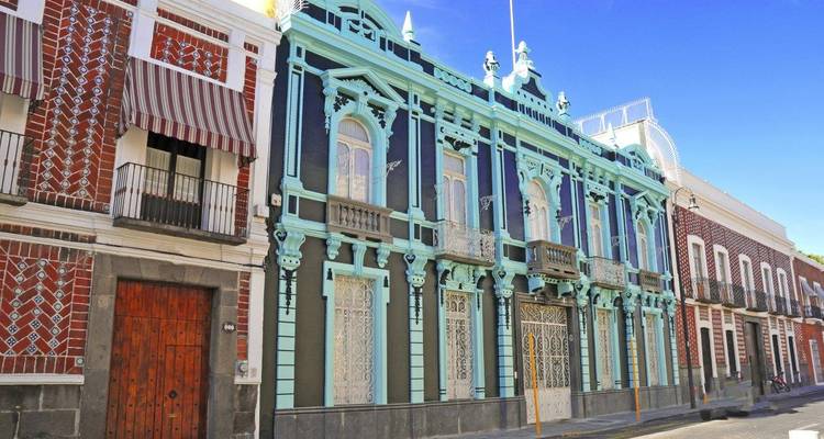 Levendige turkooizen en bakstenen koloniale gebouwen staan in een rij langs een zonnige straat in Puebla.