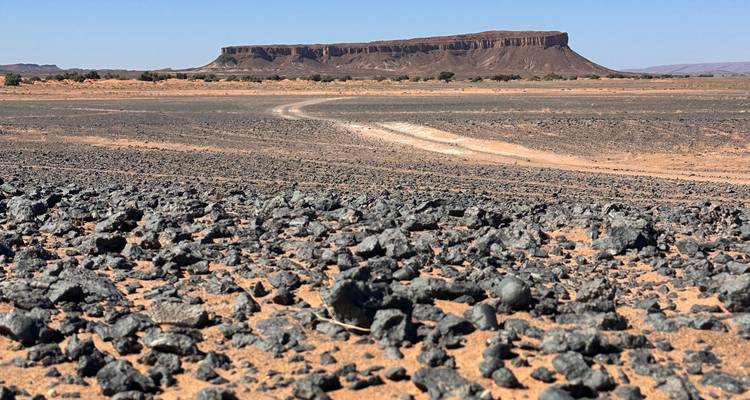 Flat-topped butte rising above barren rocky desert terrain with rugged foreground.
