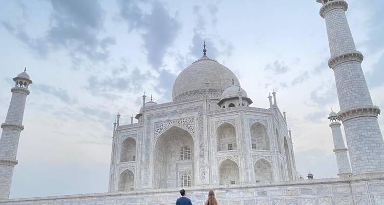 Weitaufnahme des Taj Mahal in der Morgenröte mit einem Paar, das auf einer Marmorplattform steht.
