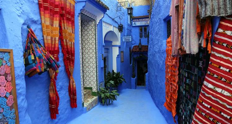 Eine lebendige blaue Gasse in Chefchaouen, gesäumt mit Textilien und Pflanzen, die eine charmante Szenerie schaffen.