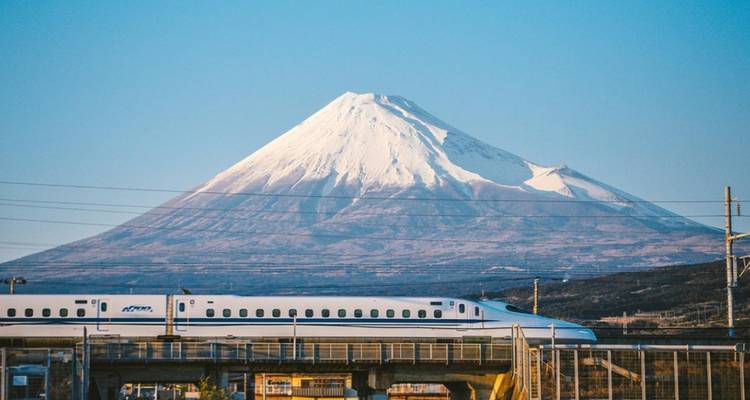 Hochgeschwindigkeitszug Shinkansen, der an schneebedecktem Berg Fuji unter blauem Himmel vorbeifährt