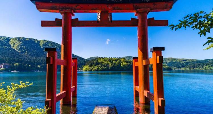 Vermilion torii gate of Hakone Shrine standing over the tranquil waters of Lake Ashi.
