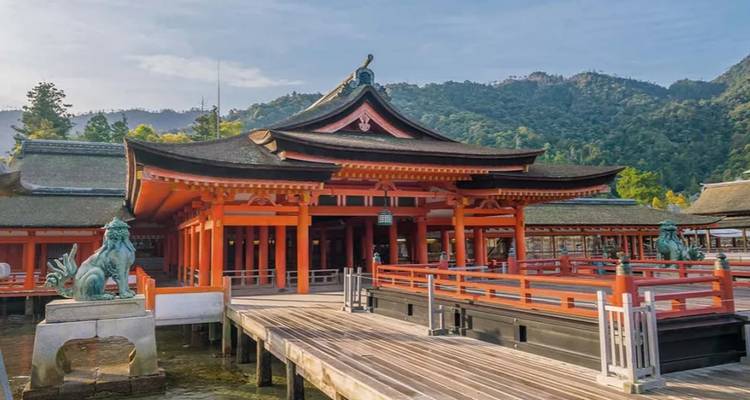 Historic Itsukushima Shrine’s bright red halls built over the water with forested hills behind.