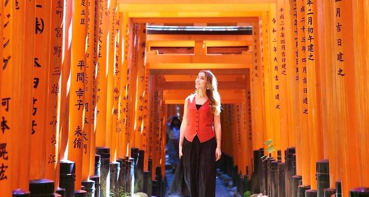 Woman walking through the endless vermilion torii tunnels of Fushimi Inari Shrine.