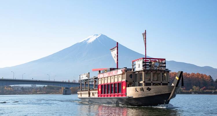 Traditional river boat cruising on Lake Kawaguchiko with snow-capped Mount Fuji towering behind.