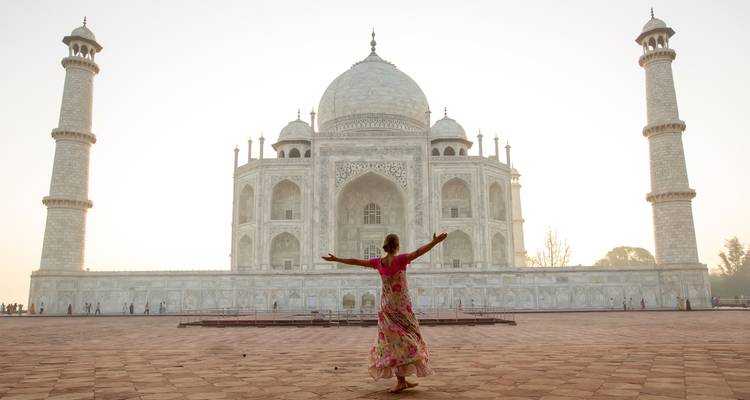 A joyful woman spreads her arms in front of the Taj Mahal at soft sunrise light.