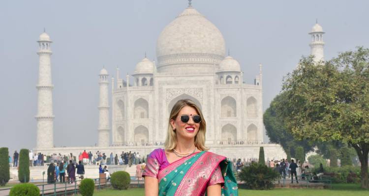 Smiling traveler in colorful sari poses with the Taj Mahal looming behind her.