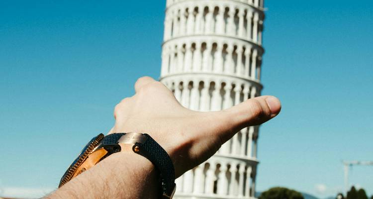 Creatief perspectief van een hand die doet alsof hij de Toren van Pisa omhoog houdt tegen een heldere lucht.