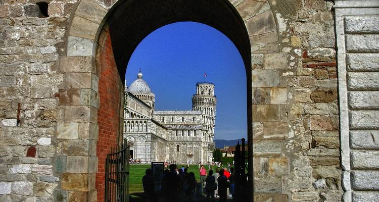 Kathedraal van Pisa en de Scheve Toren omlijst door een stenen boog met bezoekers eronder.