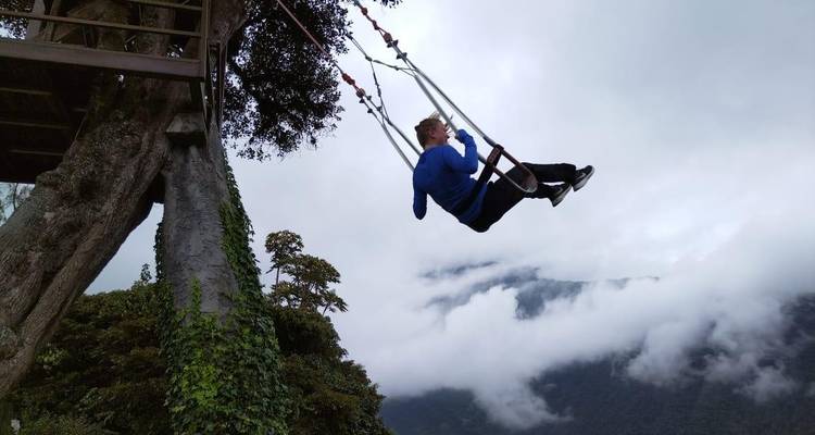 Traveler on a swing suspended from a tree high over misty cloud-covered mountains in Baños.